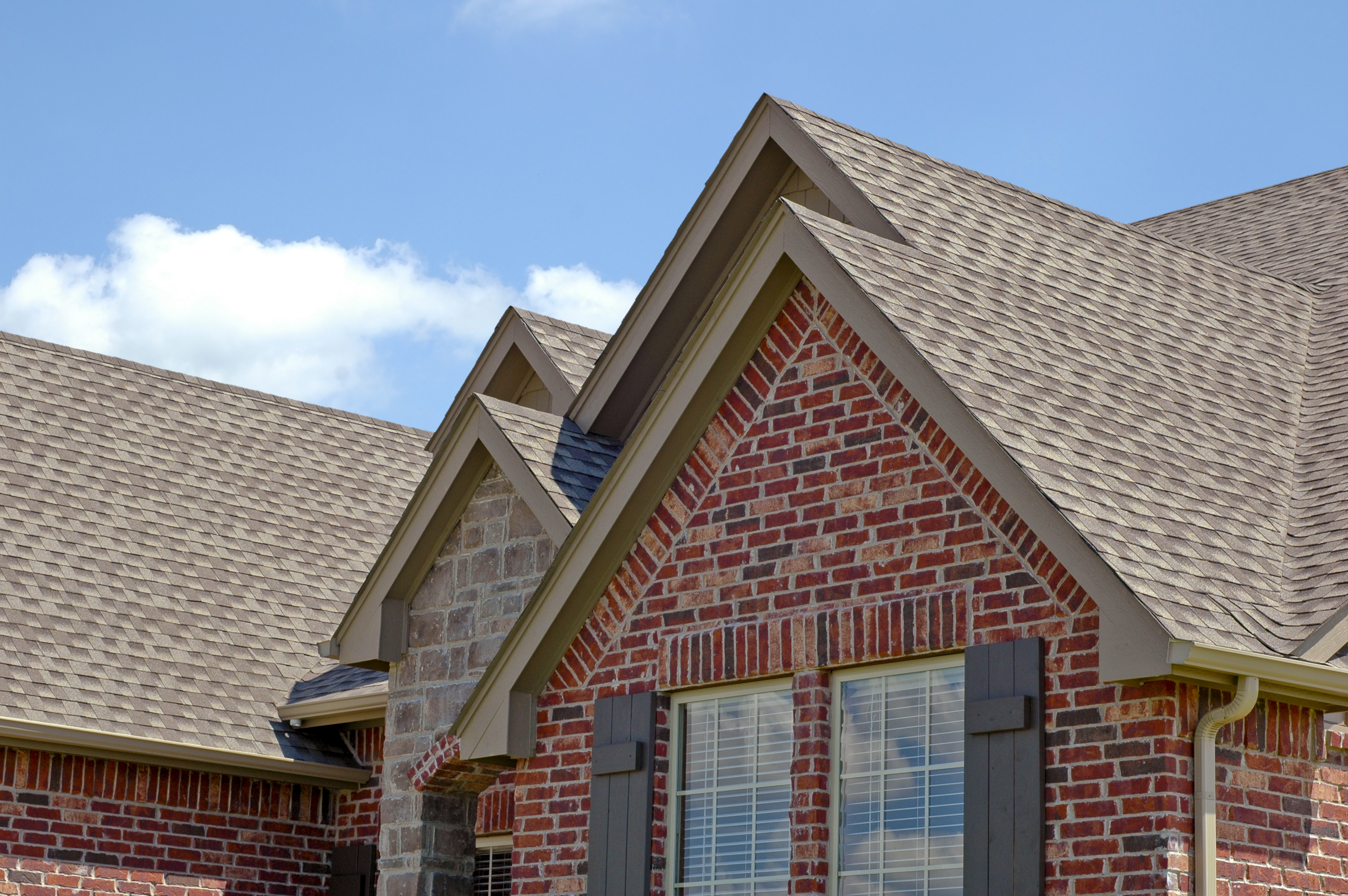 Close-up of a house roof with brick walls and dormer windows under a blue sky.