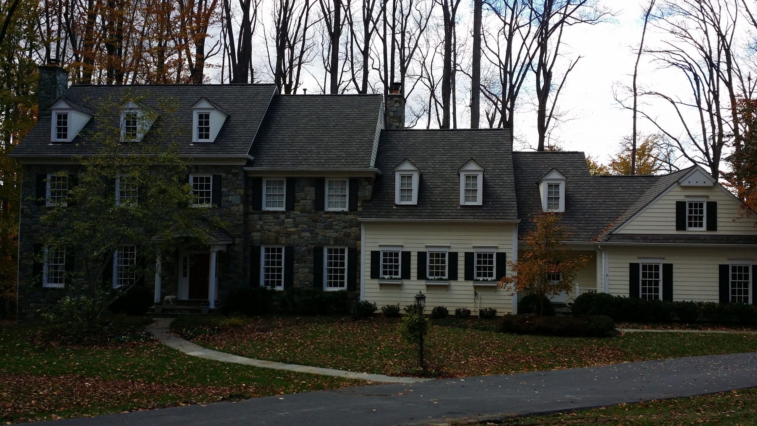 A charming stone house with dormer windows surrounded by tall leafless trees.