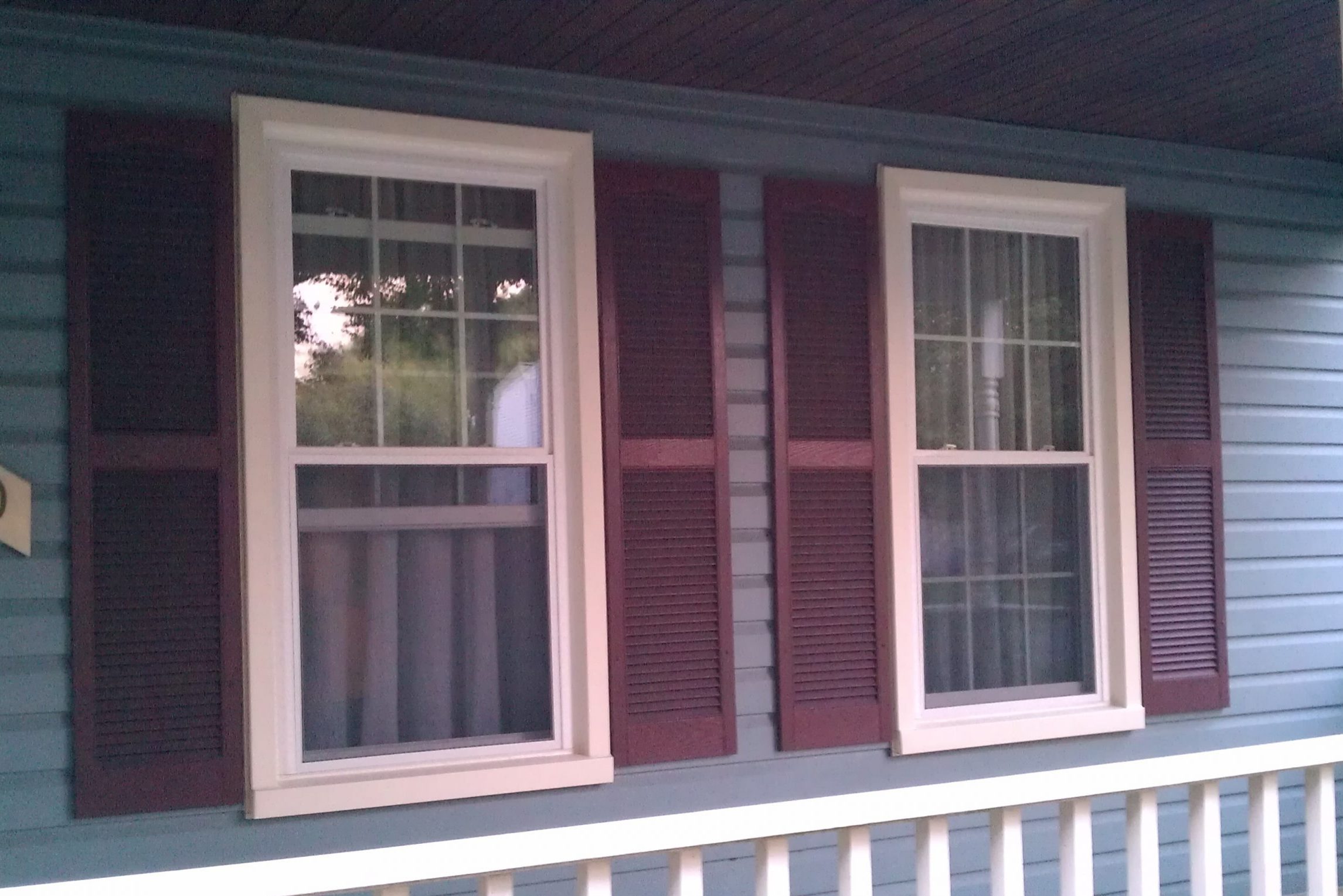 Two windows with white frames and red shutters on a house exterior.